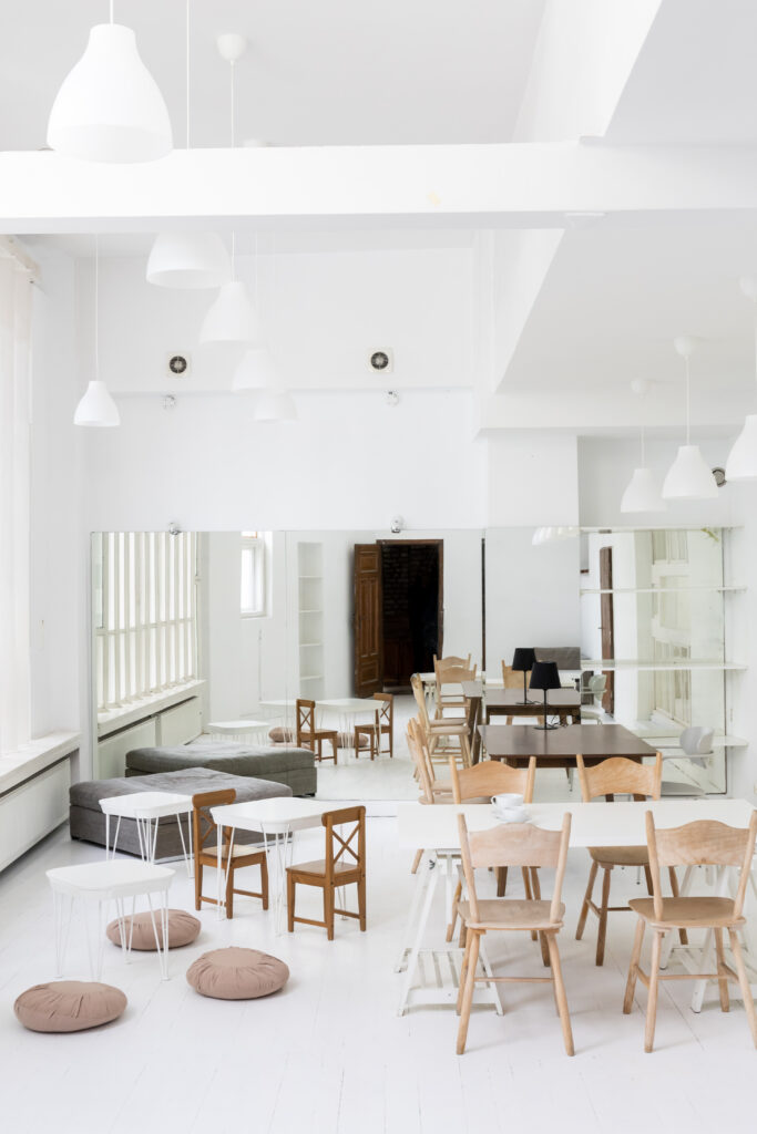 Sala edukacyjna w Hashtag Labie, białe ściany i podłoga, wyposażona w stoły i krzesła, na końcu pomieszczenia - lustro